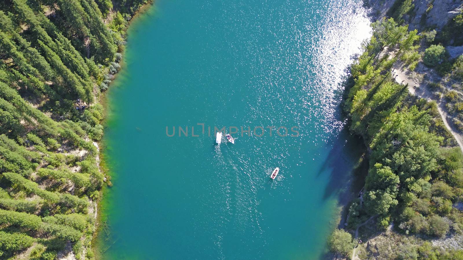 Kolsay lake among green hills and mountains. The mountain lake is surrounded by green forest, tall coniferous trees, grass and bushes. Clean water is like a mirror. Tourists swim on boats. Kazakhstan