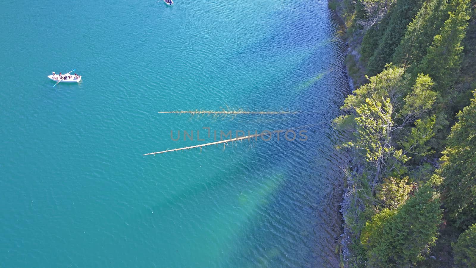 Kolsay lake among green hills and mountains. The mountain lake is surrounded by green forest, tall coniferous trees, grass and bushes. Clean water is like a mirror. Tourists swim on boats. Kazakhstan