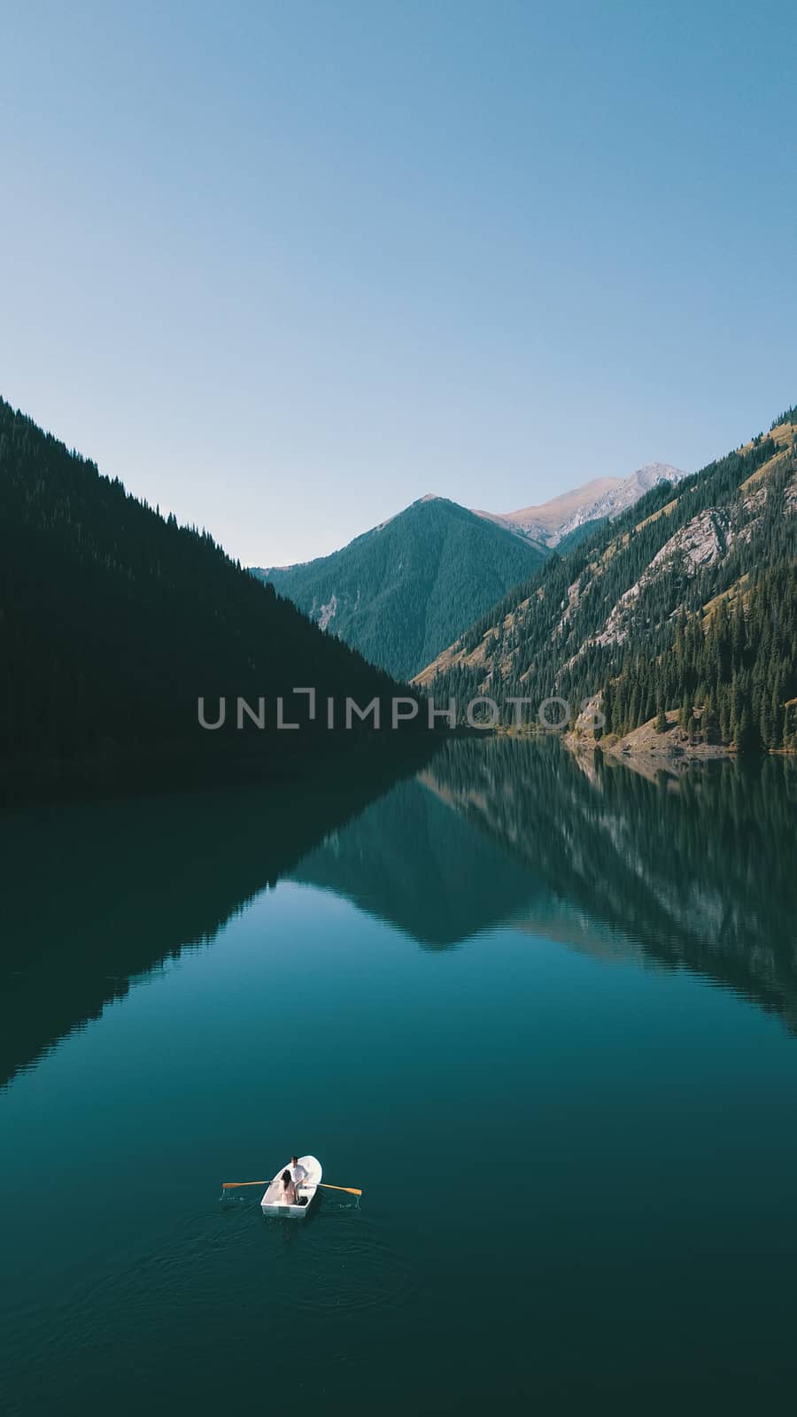 Kolsay lake among green hills and mountains. The mountain lake is surrounded by green forest, tall coniferous trees, grass and bushes. Clean water is like a mirror. Tourists swim on boats. Kazakhstan