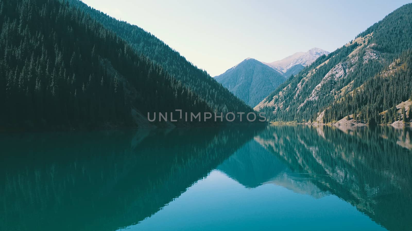 Kolsay lake among green hills and mountains. The mountain lake is surrounded by green forest, tall coniferous trees, grass and bushes. Clean water is like a mirror. Tourists swim on boats. Kazakhstan