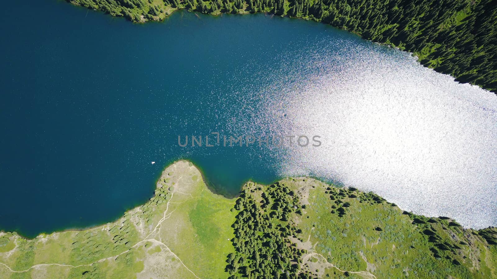 Kolsay lake among green hills and mountains. The mountain lake is surrounded by green forest, tall coniferous trees, grass and bushes. Clean water is like a mirror. Tourists swim on boats. Kazakhstan