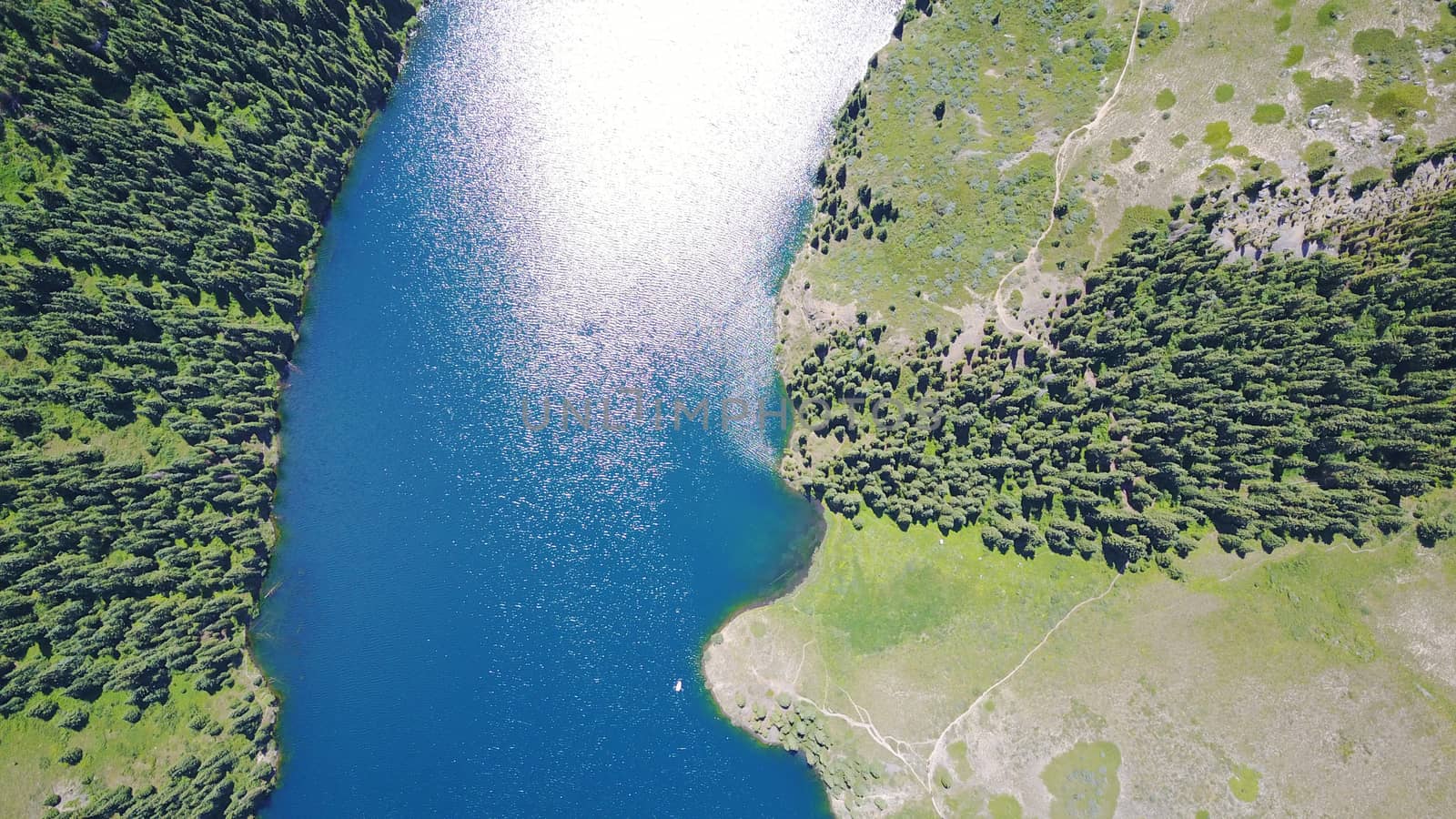 Kolsay lake among green hills and mountains. The mountain lake is surrounded by green forest, tall coniferous trees, grass and bushes. Clean water is like a mirror. Tourists swim on boats. Kazakhstan