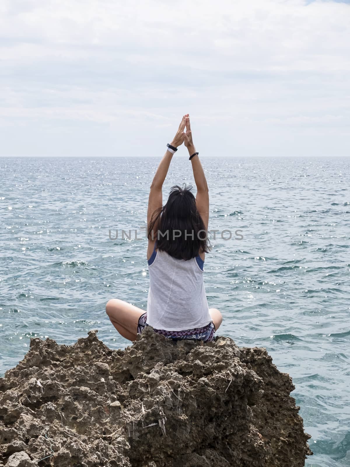 Rear view of young woman with long hair practicing yoga on rocks at sea