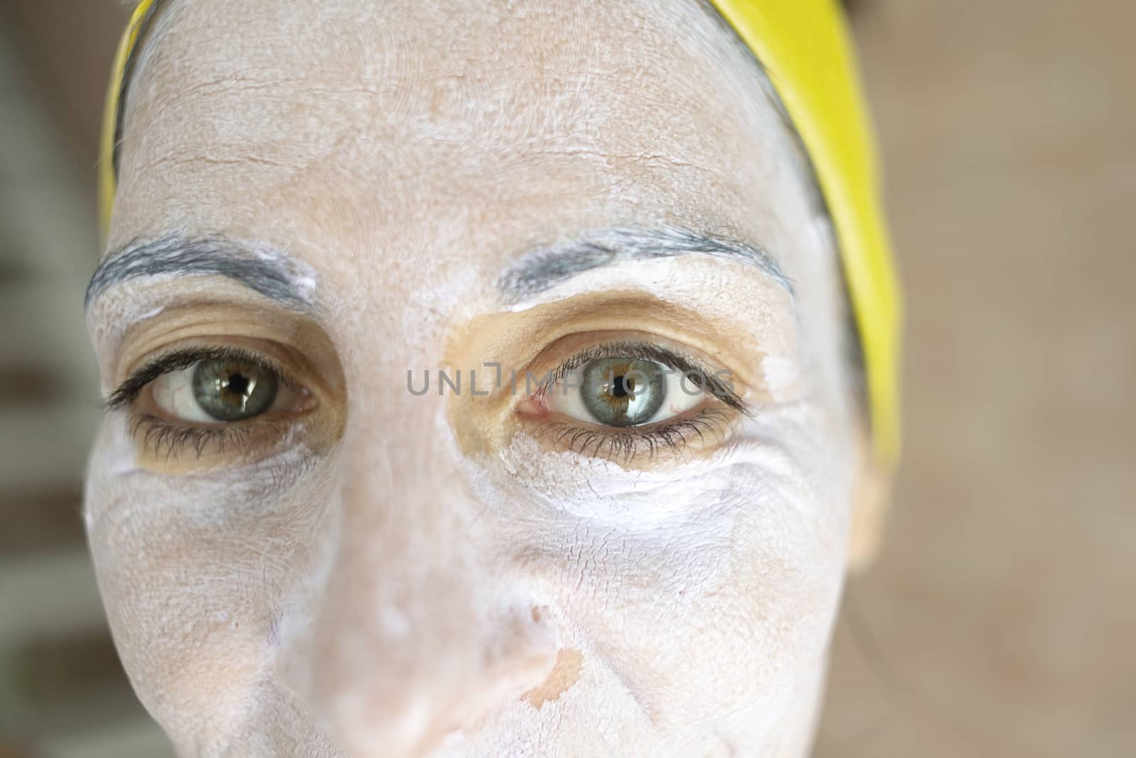 Relaxed woman applies mineral clay mask on face for rejuvenation, has headband on head