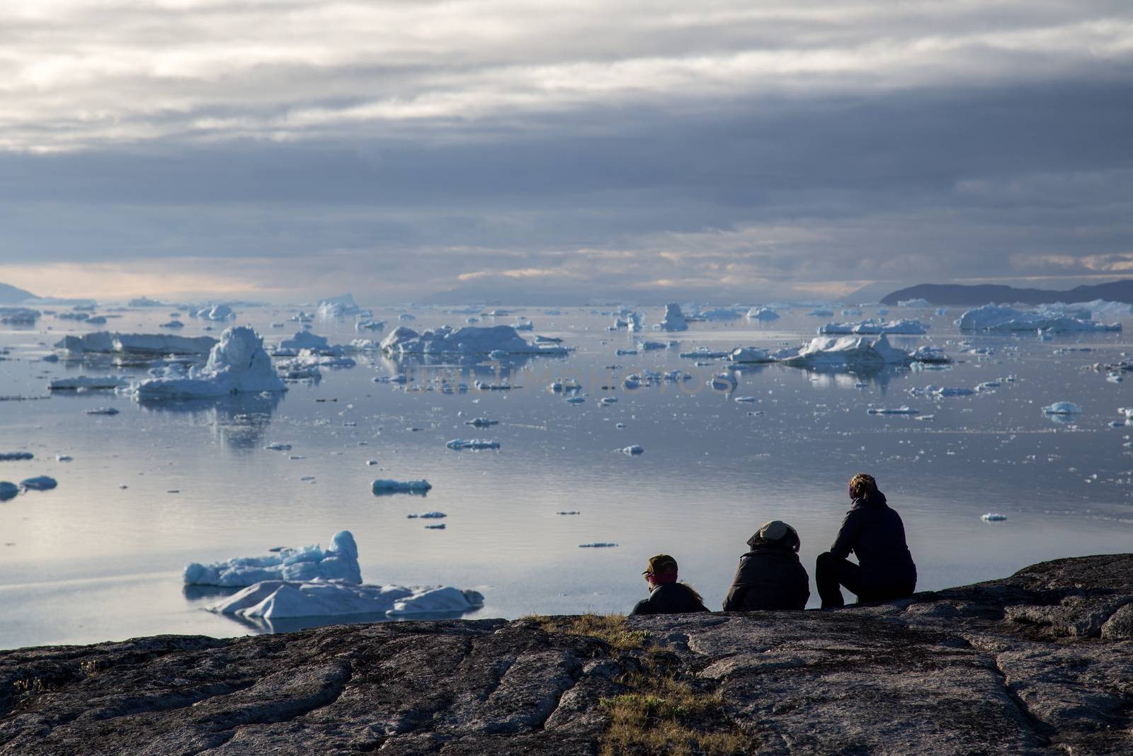Rodebay, Greenland - July 09, 2018: A group of people sitting and looking at icebergs. Rodebay, also known as Oqaatsut is a fishing settlement north of Ilulissat.