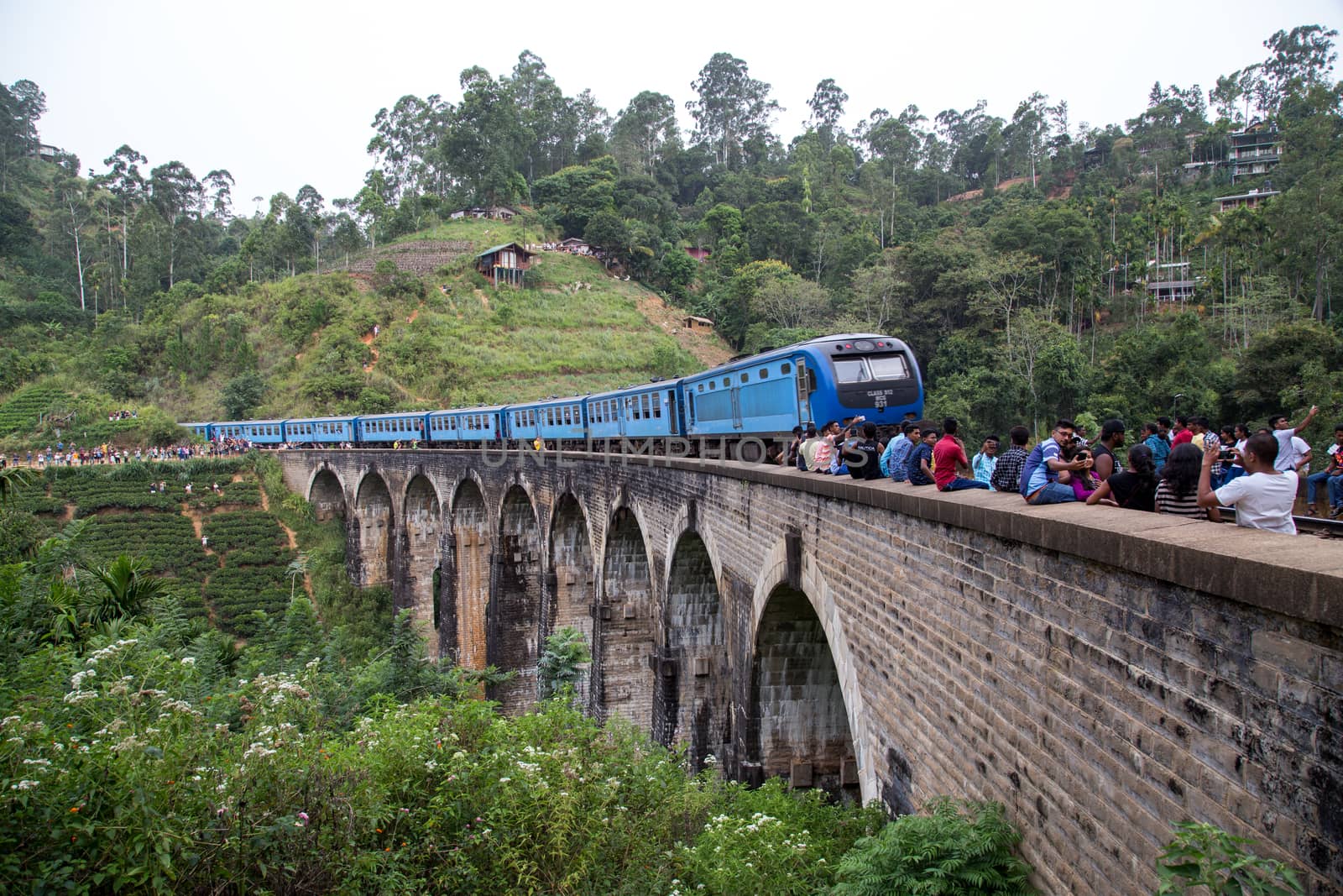 Demodara, Sri Lanka - August 5, 2018: People next to a blue train crossing the famous Nine Arch Bridge