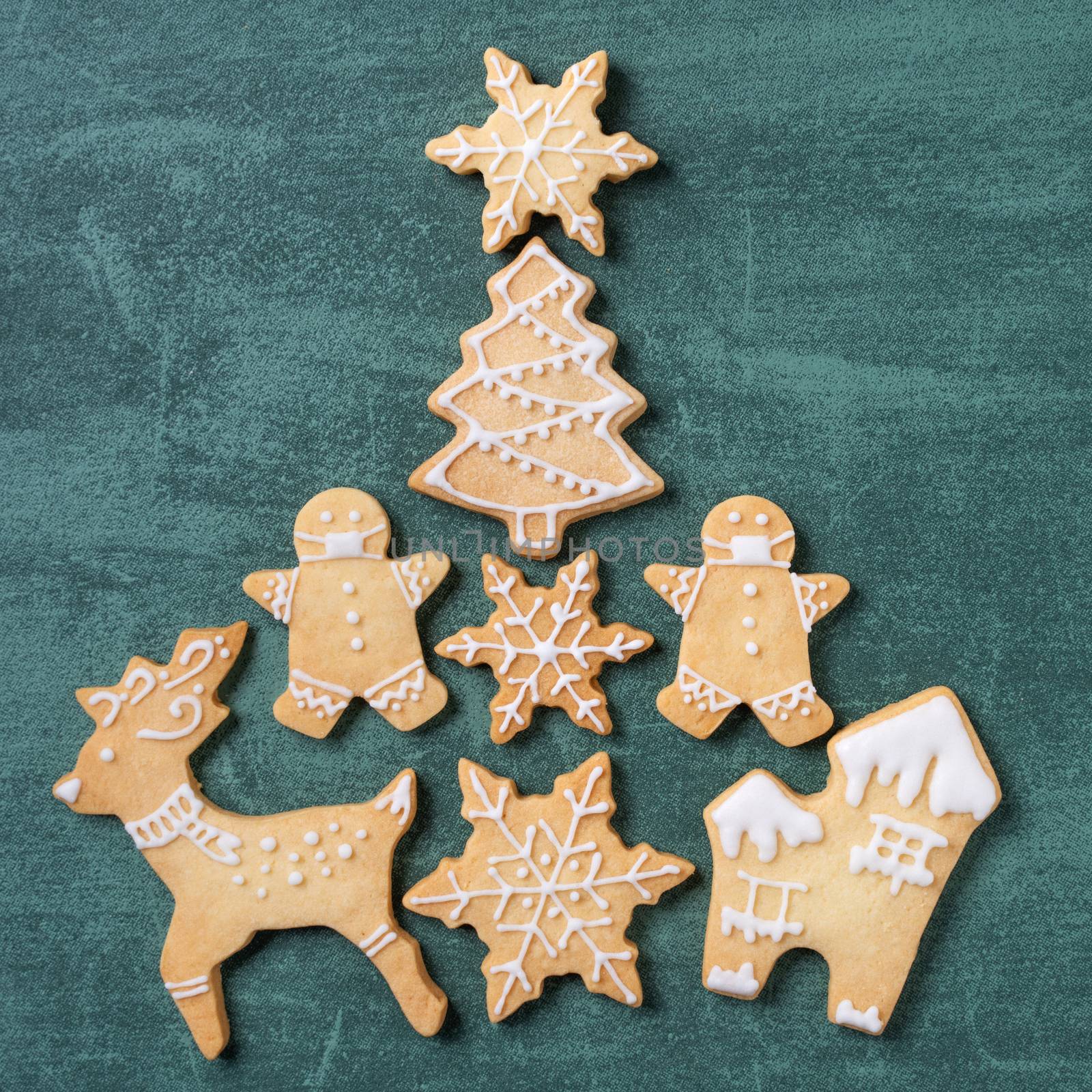 Top view of Christmas tree and snowflake cooikes with gingerbread man wearing mask on green table background.