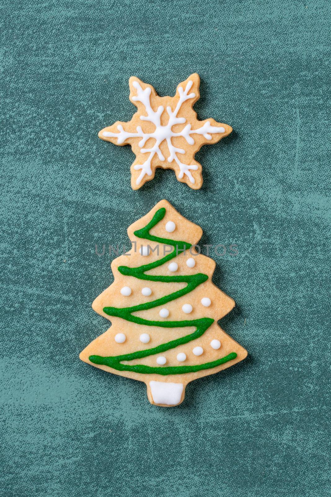 Top view of Christmas tree and snowflake cooikes with gingerbread man wearing mask on green table background.