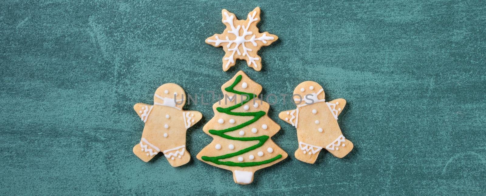 Top view of Christmas tree and snowflake cooikes with gingerbread man wearing mask on green table background.