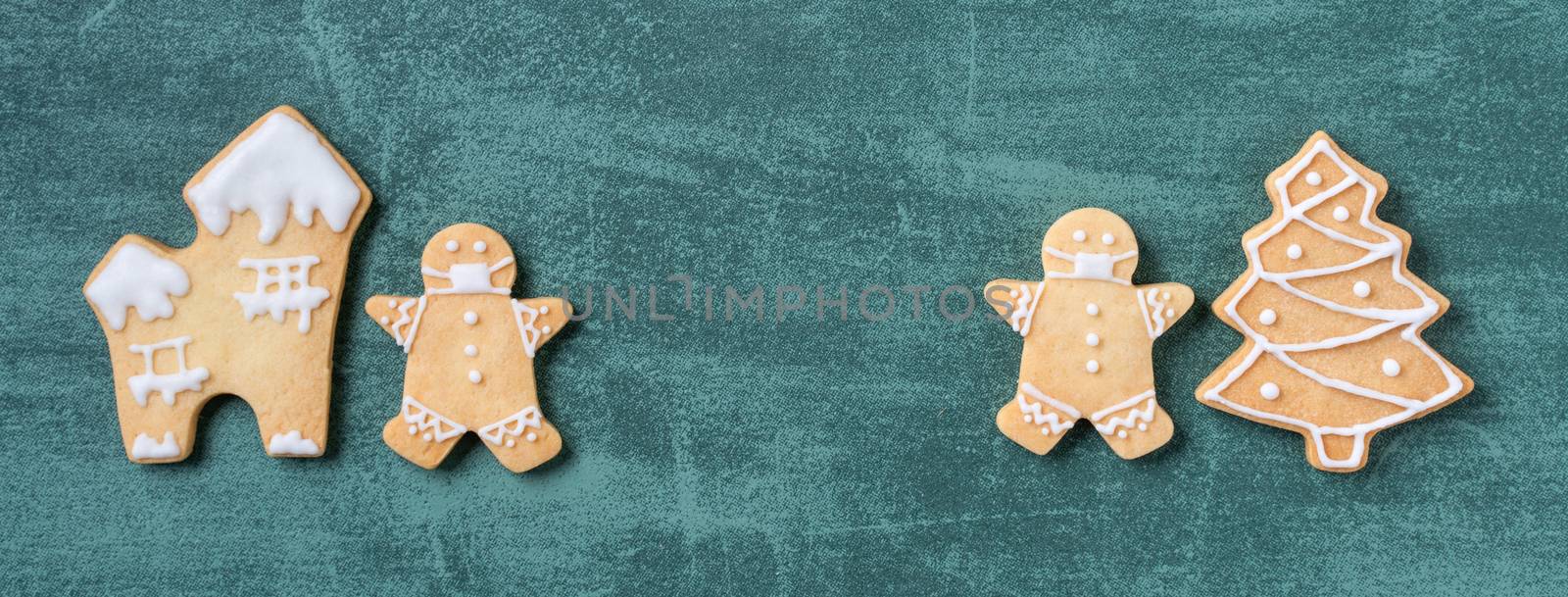 Top view of Christmas tree and snowflake cooikes with gingerbread man wearing mask on green table background.