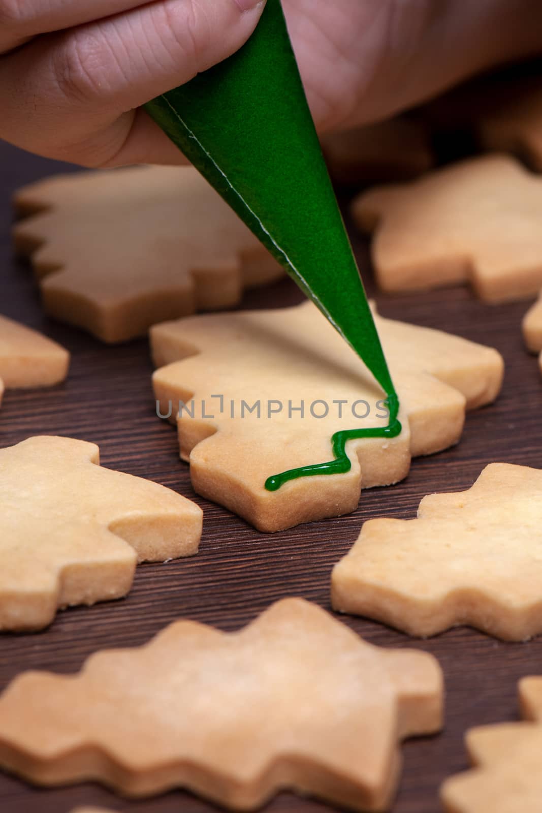 Close up of drawing gingerbread Christmas tree sugar cookie on wooden table background with green icing, concept of holiday celebration.
