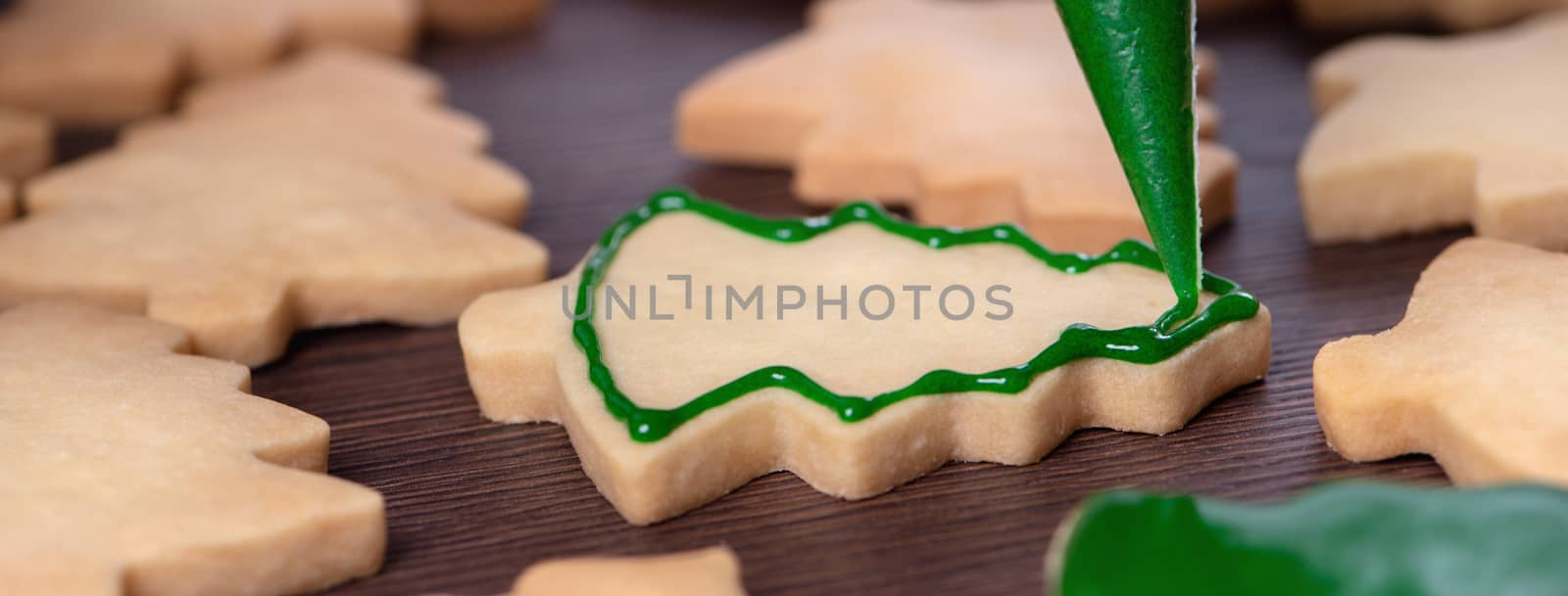 Close up of drawing gingerbread Christmas tree sugar cookie on wooden table background with green icing, concept of holiday celebration.