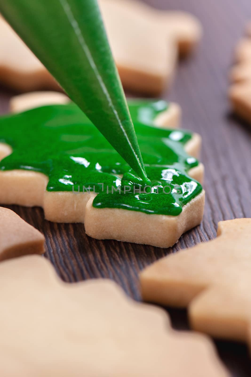 Close up of drawing gingerbread Christmas tree sugar cookie on wooden table background with green icing, concept of holiday celebration.