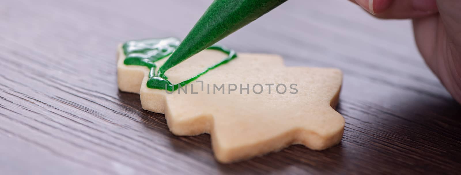 Close up of drawing gingerbread Christmas tree sugar cookie on wooden table background with green icing, concept of holiday celebration.