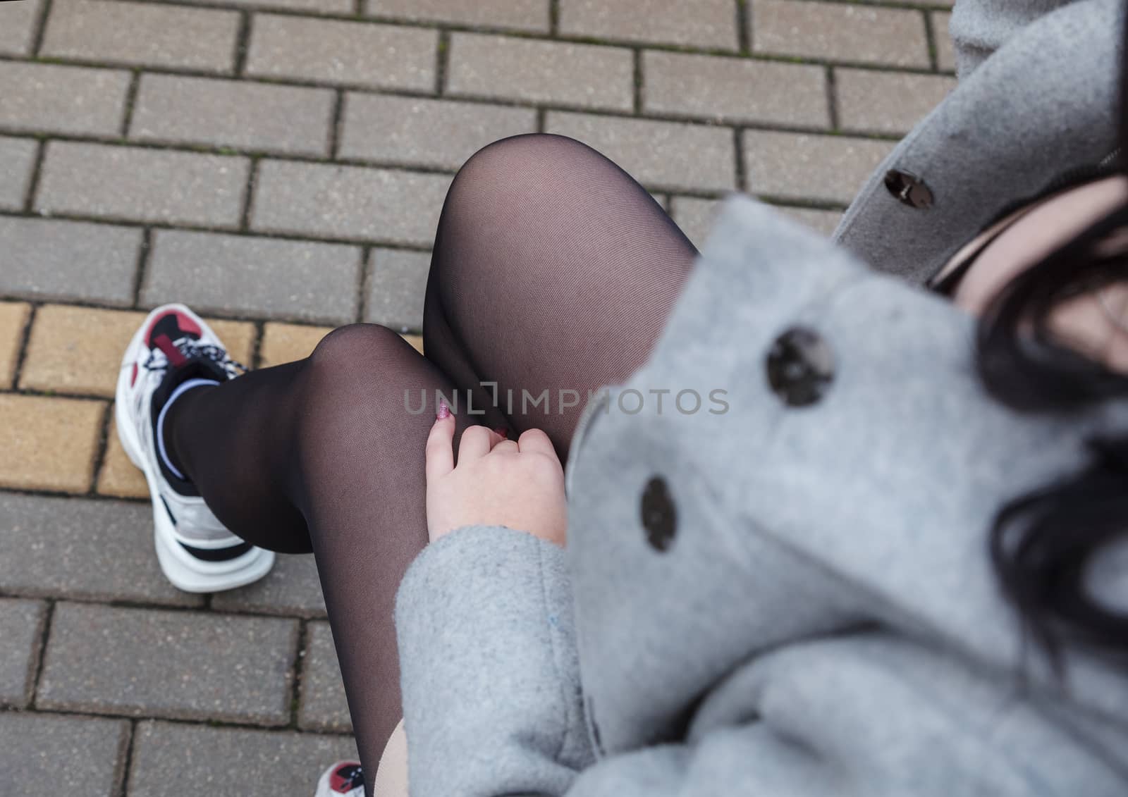 woman in gray coat sitting on a suitcase at railway station on autumn day. legs closeup