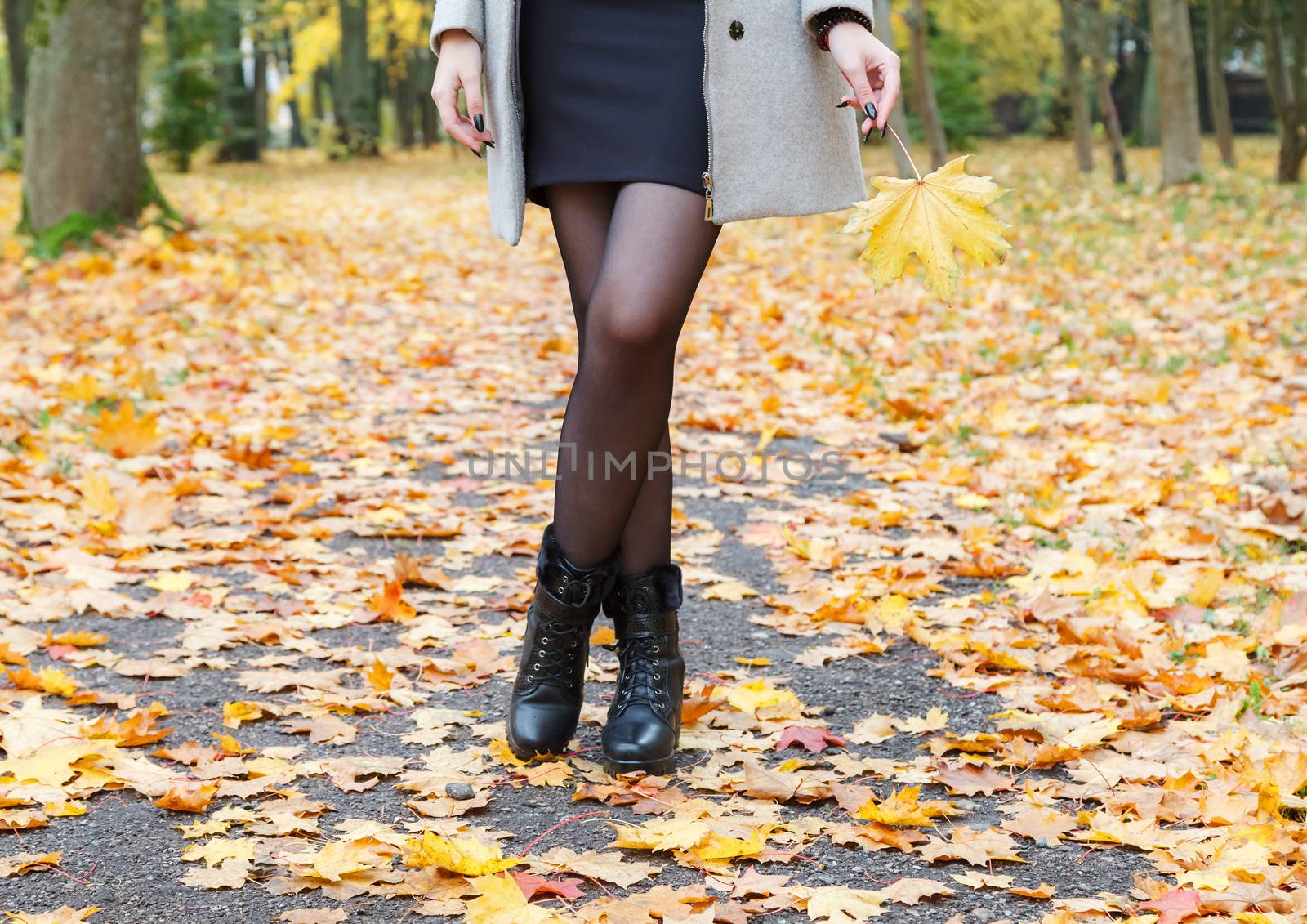 woman in gray coat standing on alley of city park on sunny autumn day. legs closeup