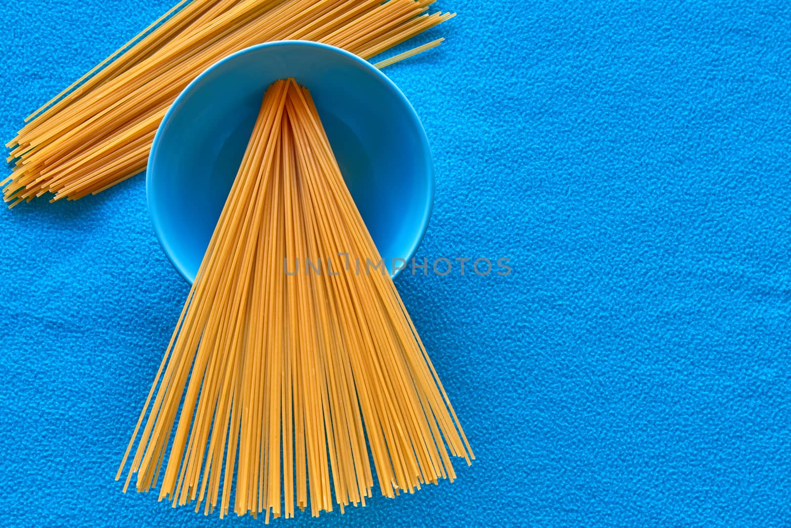 Some uncooked spaghetti in bowl with blue background