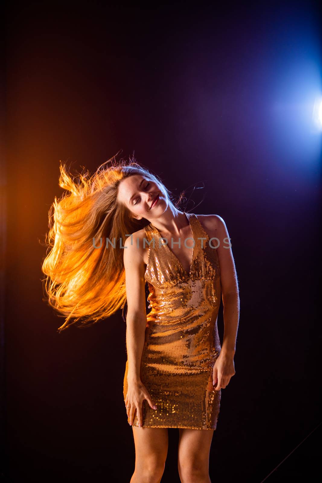 Portrait of dancing girl in golden dress on disco party blue and red studio lights