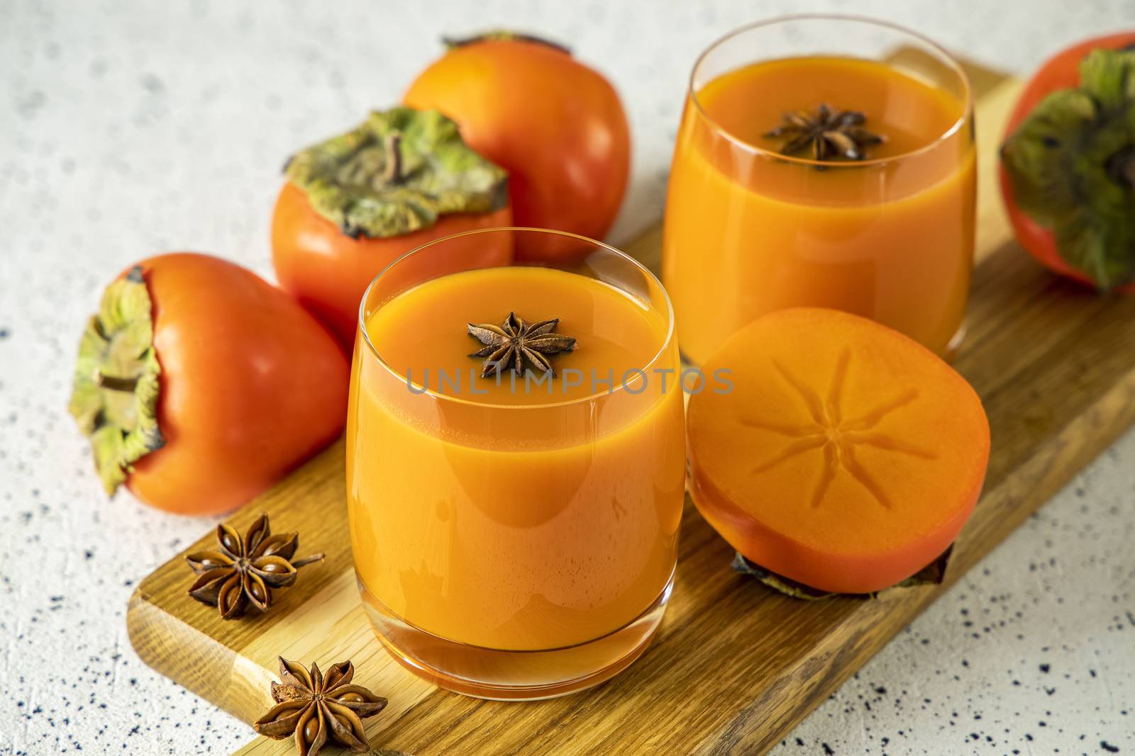 Two glasses of fresh healthy persimmon smoothie with anise stars on cutting wooden board, gray concrete background, selective focus, copy space.