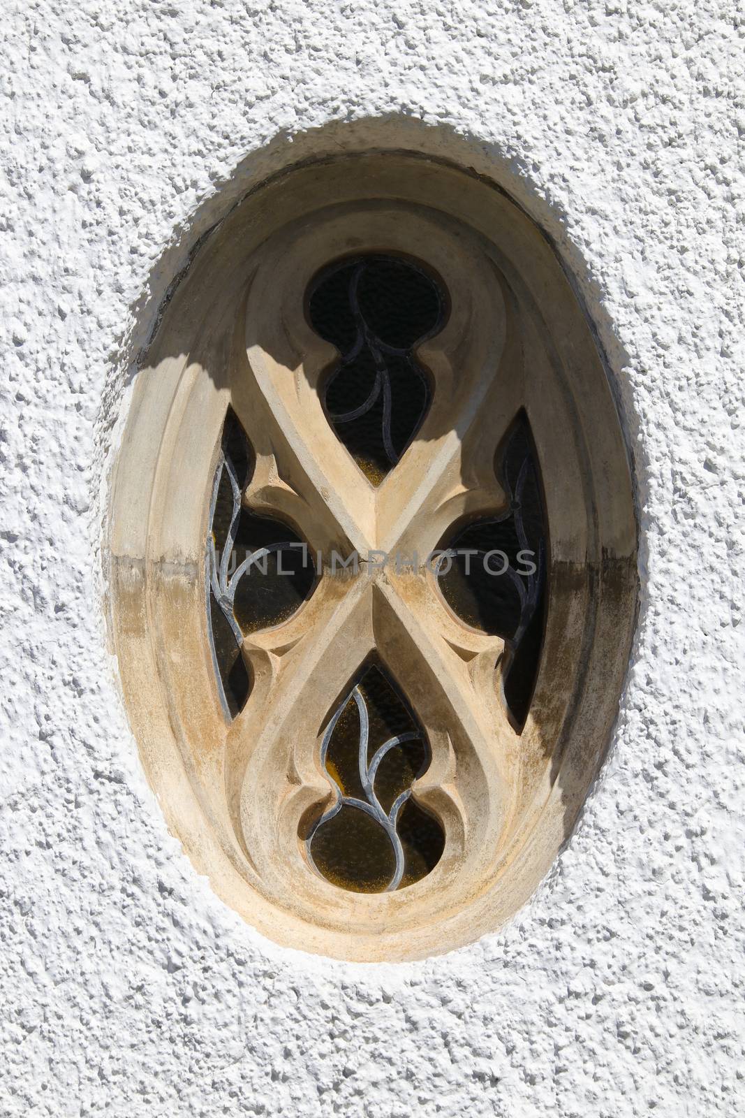 Ornate oval stone and lead glass church window with white wall, Mossel Bay, South Africa