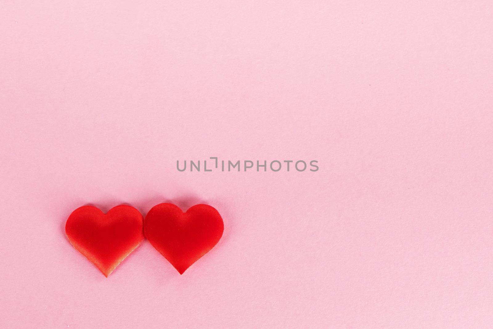 Valentine's day two red silk hearts on pink paper background, love concept