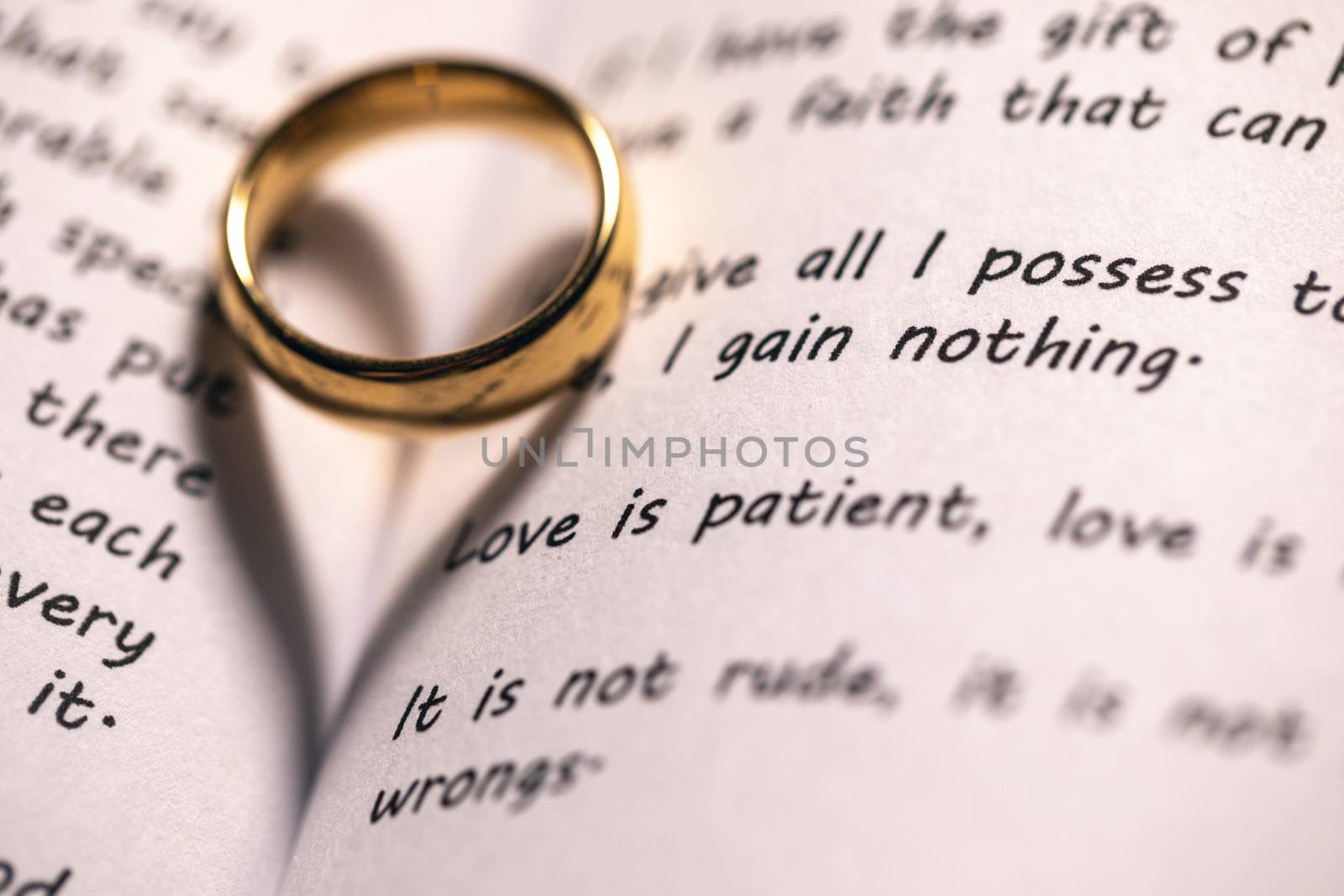 One golden wedding ring on Holy bible book with heart shaped shadow close up