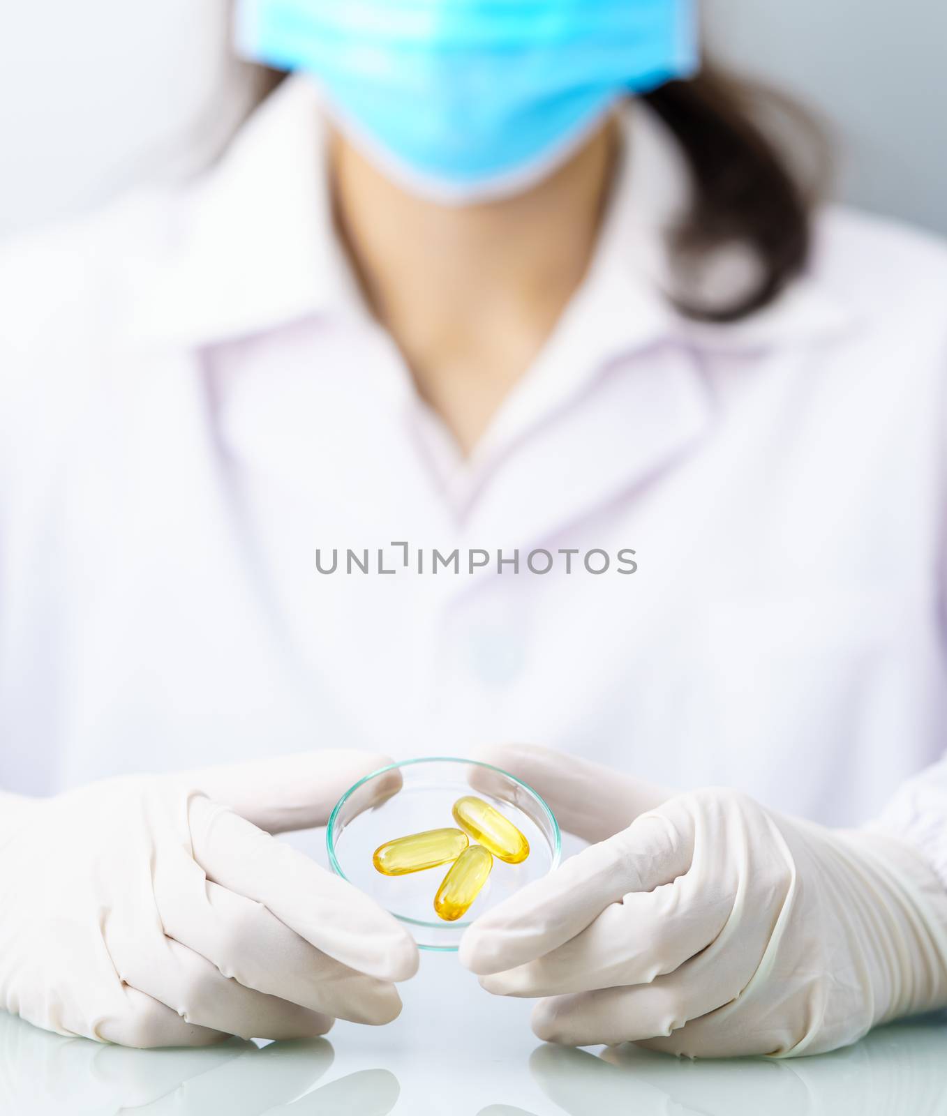 Close up Scientist hands putting in nitrile latex gloves holding Omega 3 capsule in labcoat doing experiments in lab