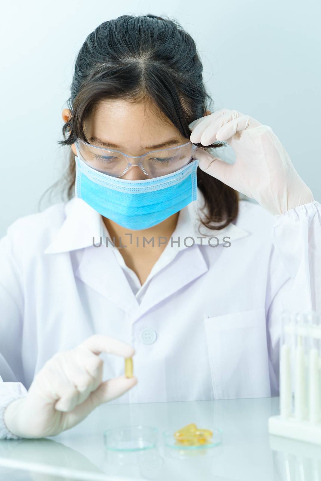 Close up Scientist hands putting in nitrile latex gloves holding Omega 3 capsule in labcoat doing experiments in lab