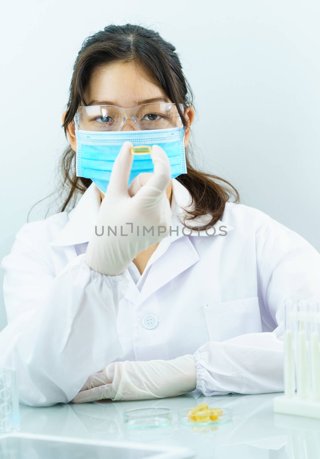 Close up Scientist hands putting in nitrile latex gloves holding Omega 3 capsule in labcoat doing experiments in lab