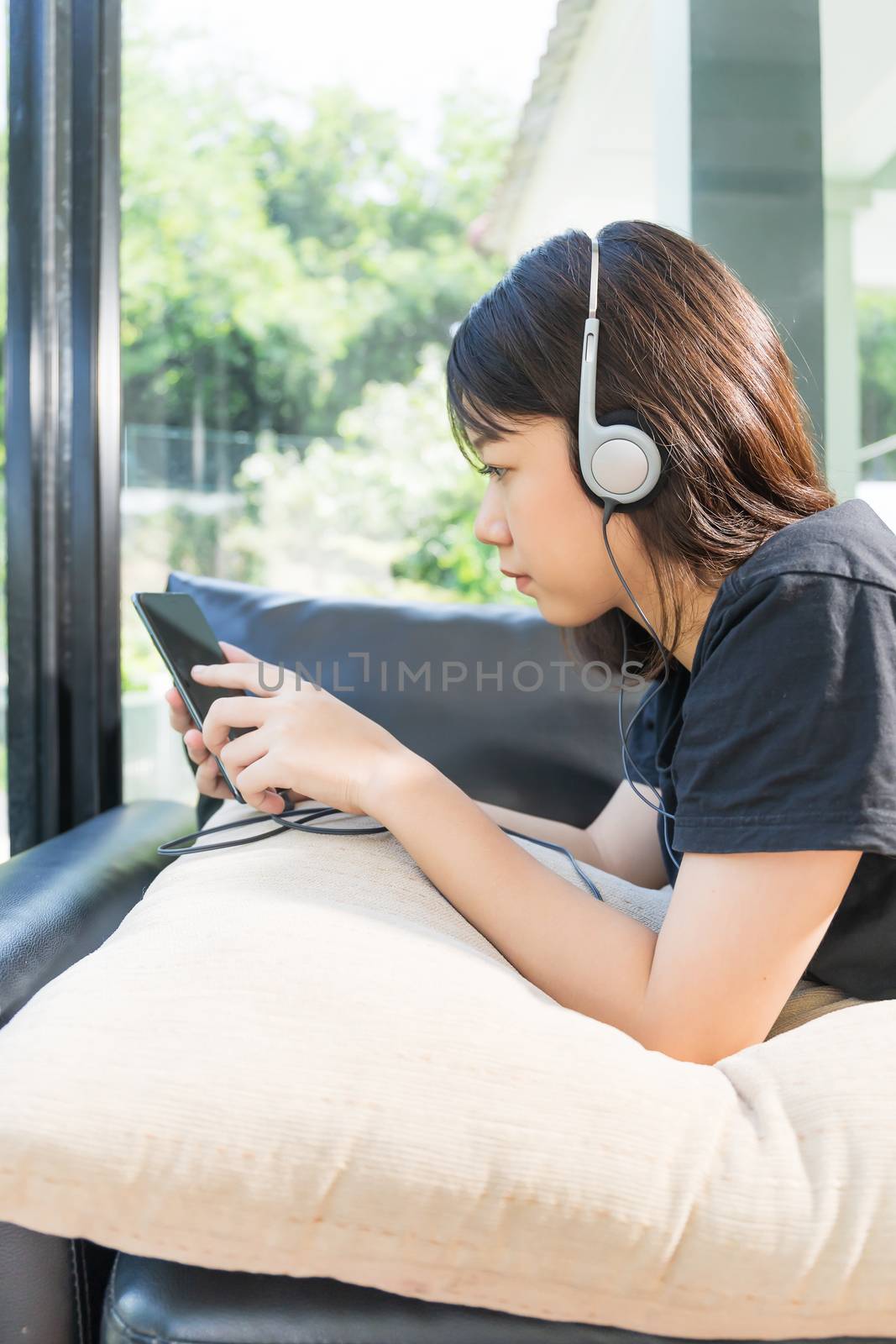 Young girl with headphones and listening to music from mobile phone on the sofa in living room at home