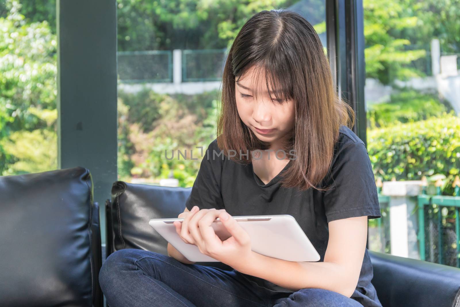 Young girl studying online from digital tablet on the sofa in parlor at home