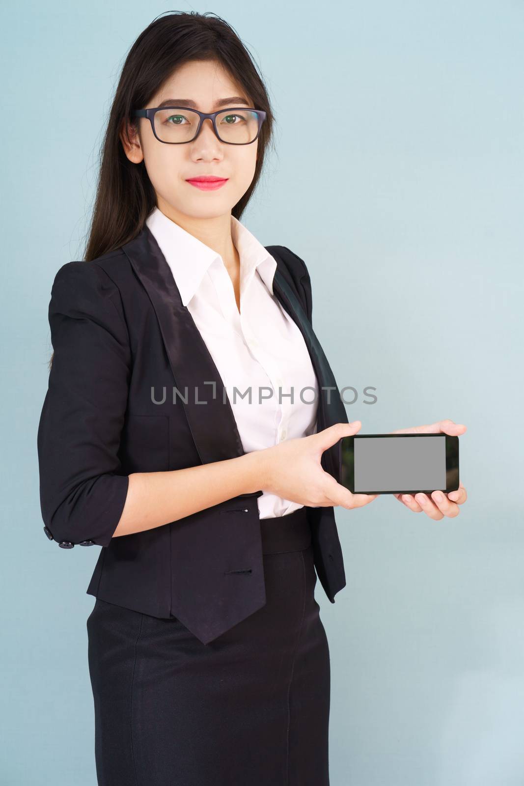 Young women in suit holding her smartphone standing against blue background