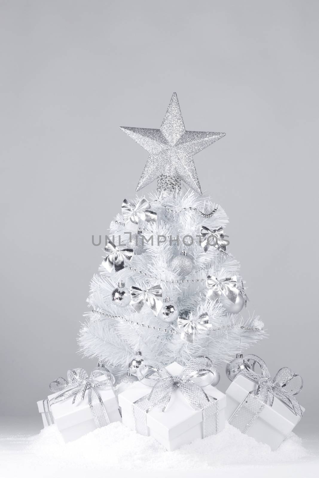 White christmas tree with silver decorations and gifts on snow on gray background