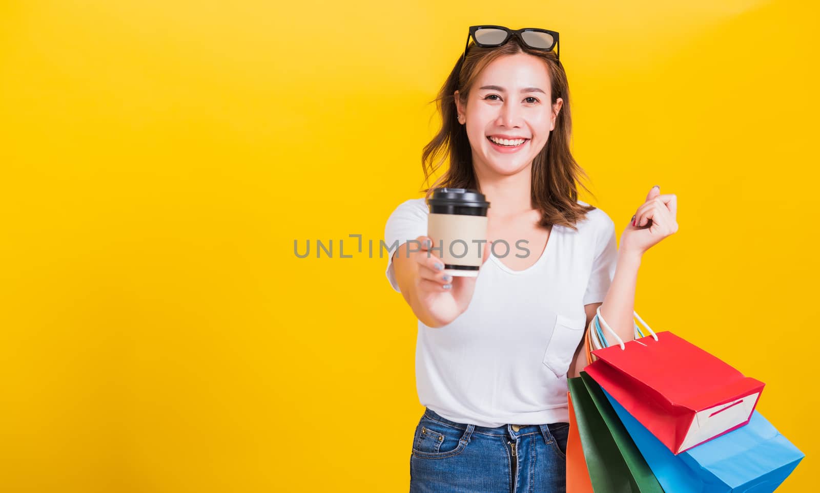 Portrait Asian Thai beautiful happy young woman smiling hold shopping bags multi-color and take away coffee cup her looking to camera, studio shot isolated on yellow background, with copy space