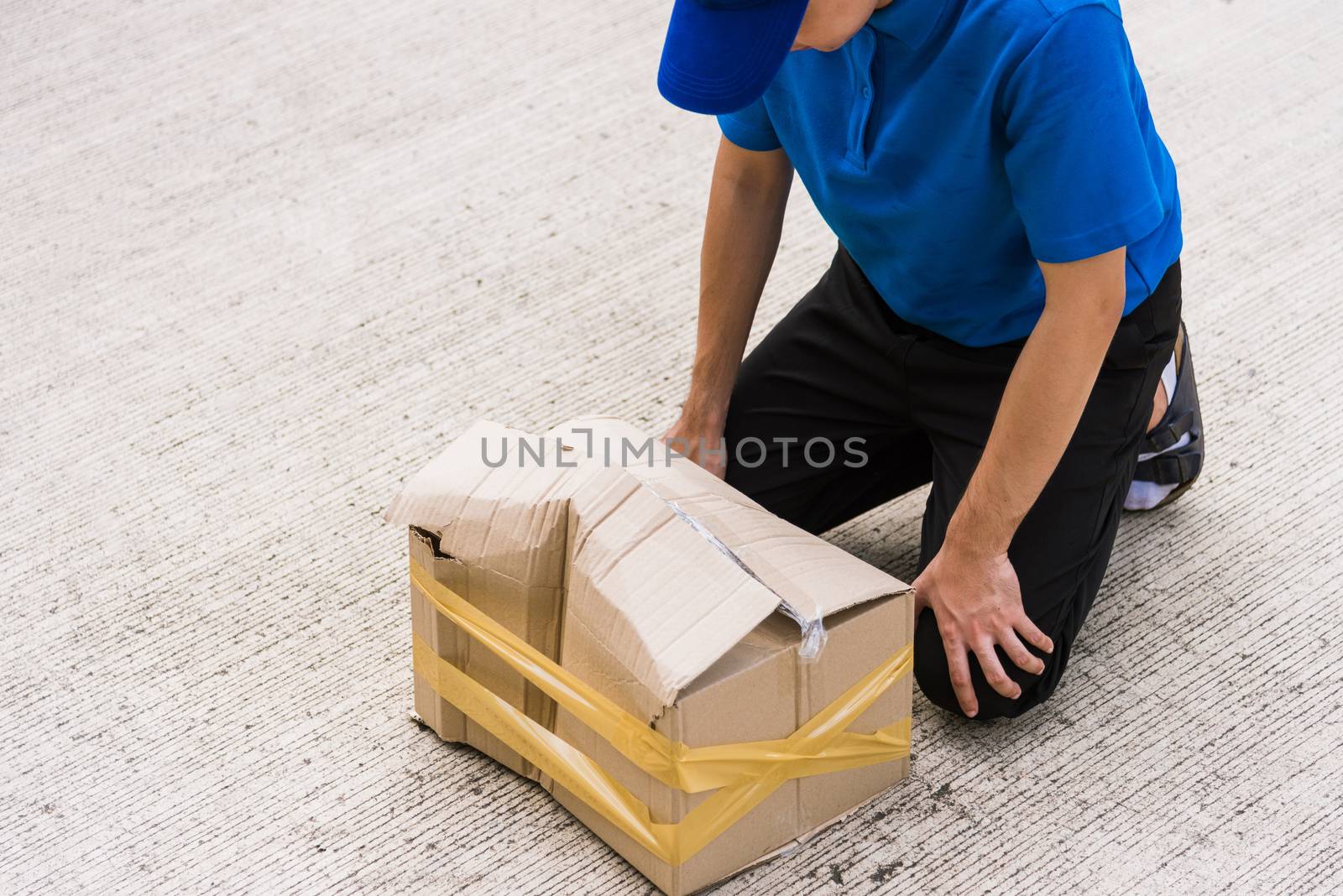 Asian young delivery man in blue uniform he emotional falling courier hold damaged cardboard box is broken at door front home, Accident bad transport shipment or poor quality delivery service concept