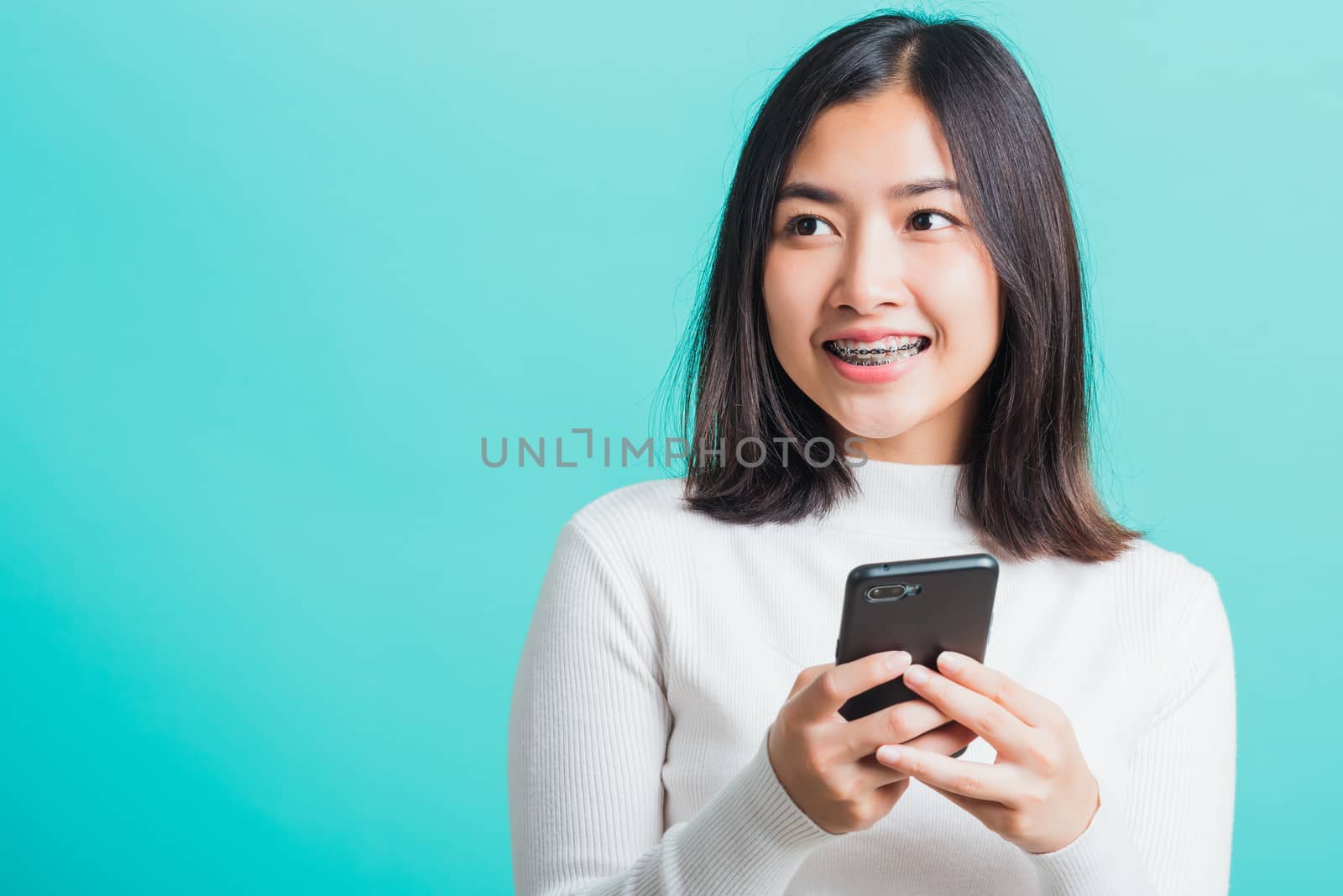 Portrait of Asian woman smile she holding and typing text message on a smartphone, female excited cheerful her reading mobile phone some social media isolated on a blue background, Technology concept