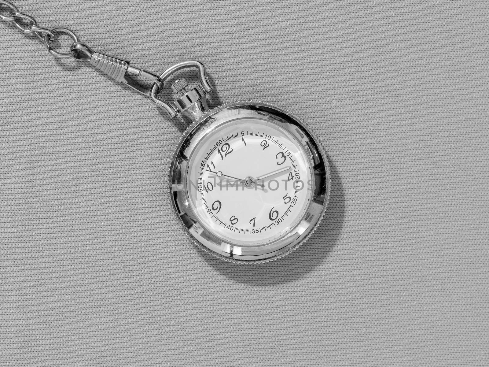 Small steel pocket watch with white dial, black and white image of metal object on uniform background