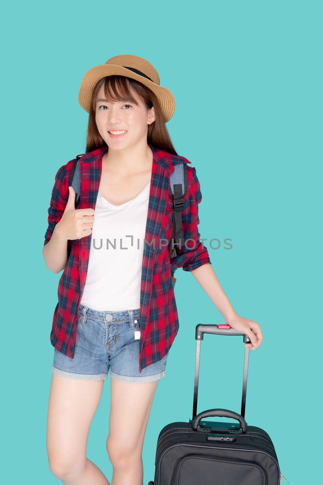 Beautiful young asian woman pulling suitcase isolated on blue background, asia girl cheerful holding luggage walking and gesture thumbs up in vacation with excited, journey and travel concept. by nnudoo