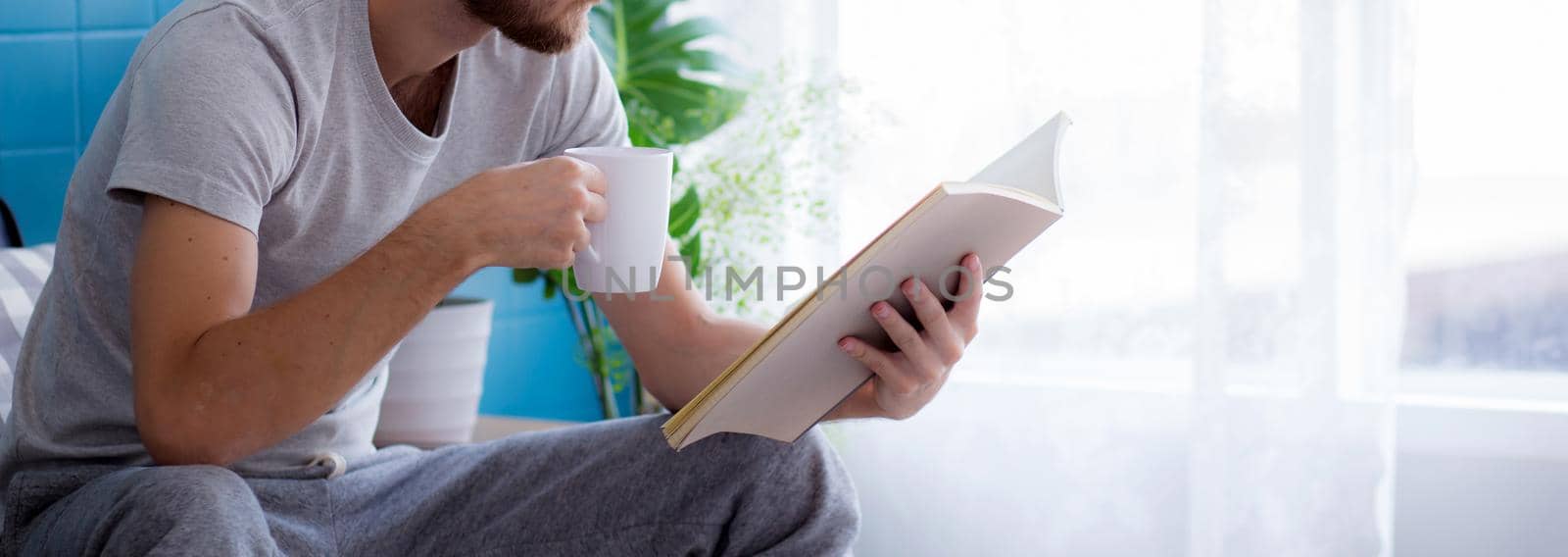 Young man reading a book sitting on sofa for rest is hobby in living room, stay home for leisure, lifestyle of new normal for social distracting, male learn and study in interesting in spare time. by nnudoo