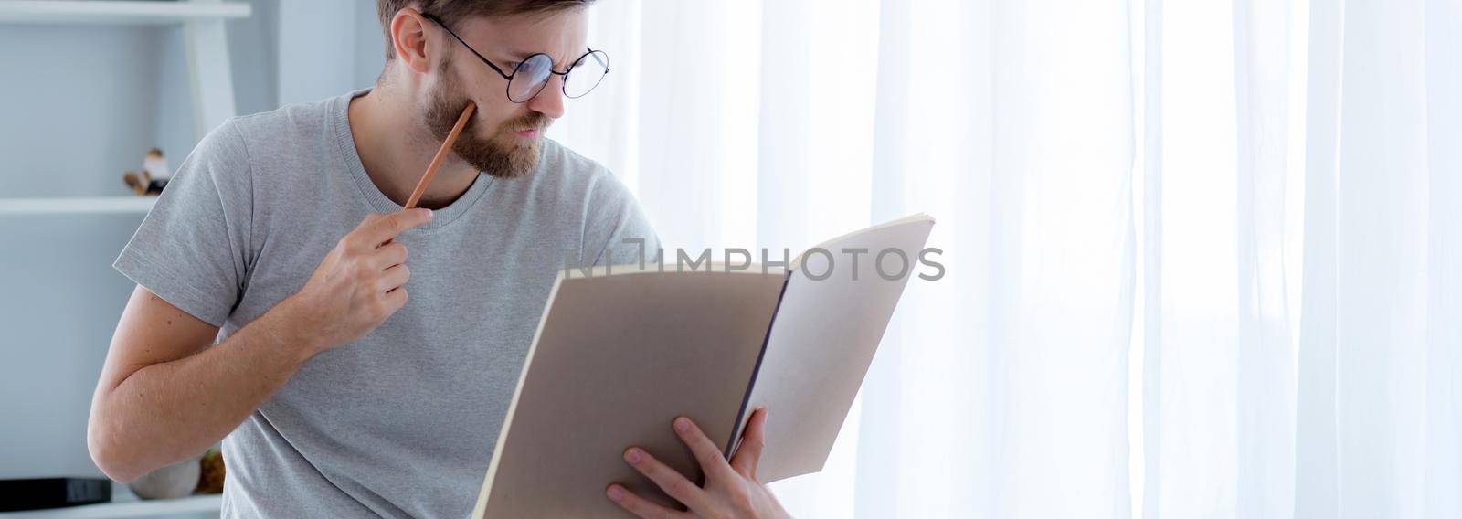 Young man reading book preparing exam at room, male learning and homework, erudition and clever, intelligent with cognition for study, knowledge and wisdom, education and lifestyle concept.