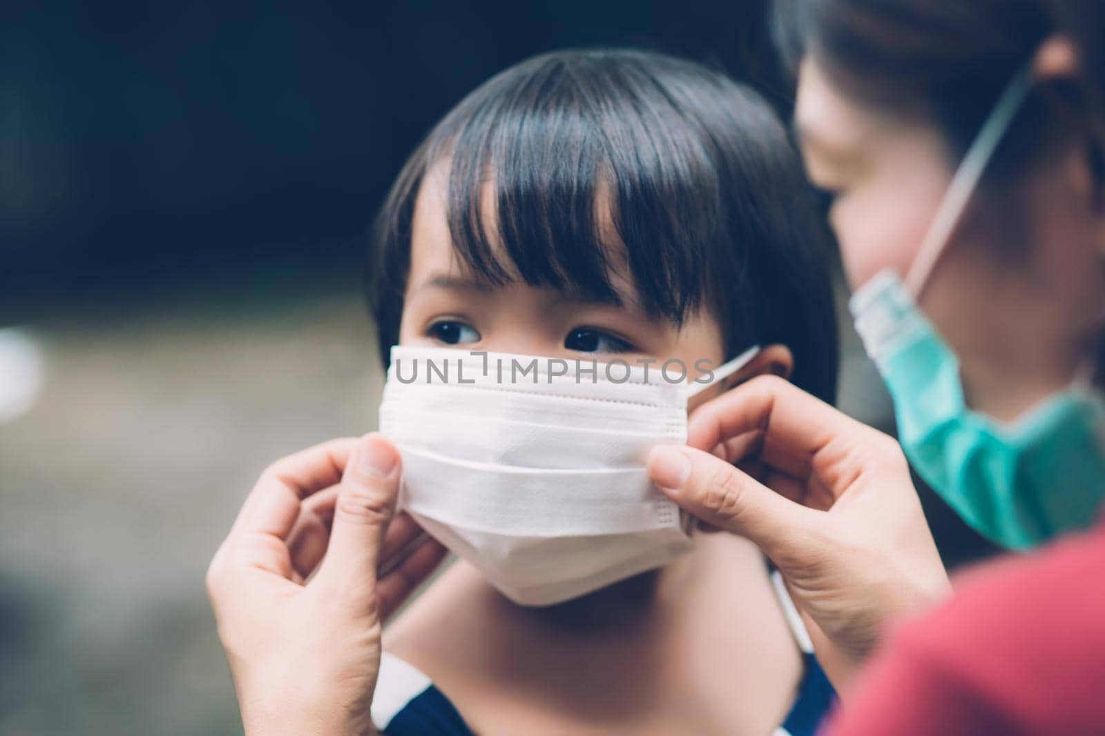 Mother take care daughter with face mask for protection disease flu or covid-19 outdoors, mom wearing on medical mask with child safety for protect outbreak of pandemic, medical concept. by nnudoo