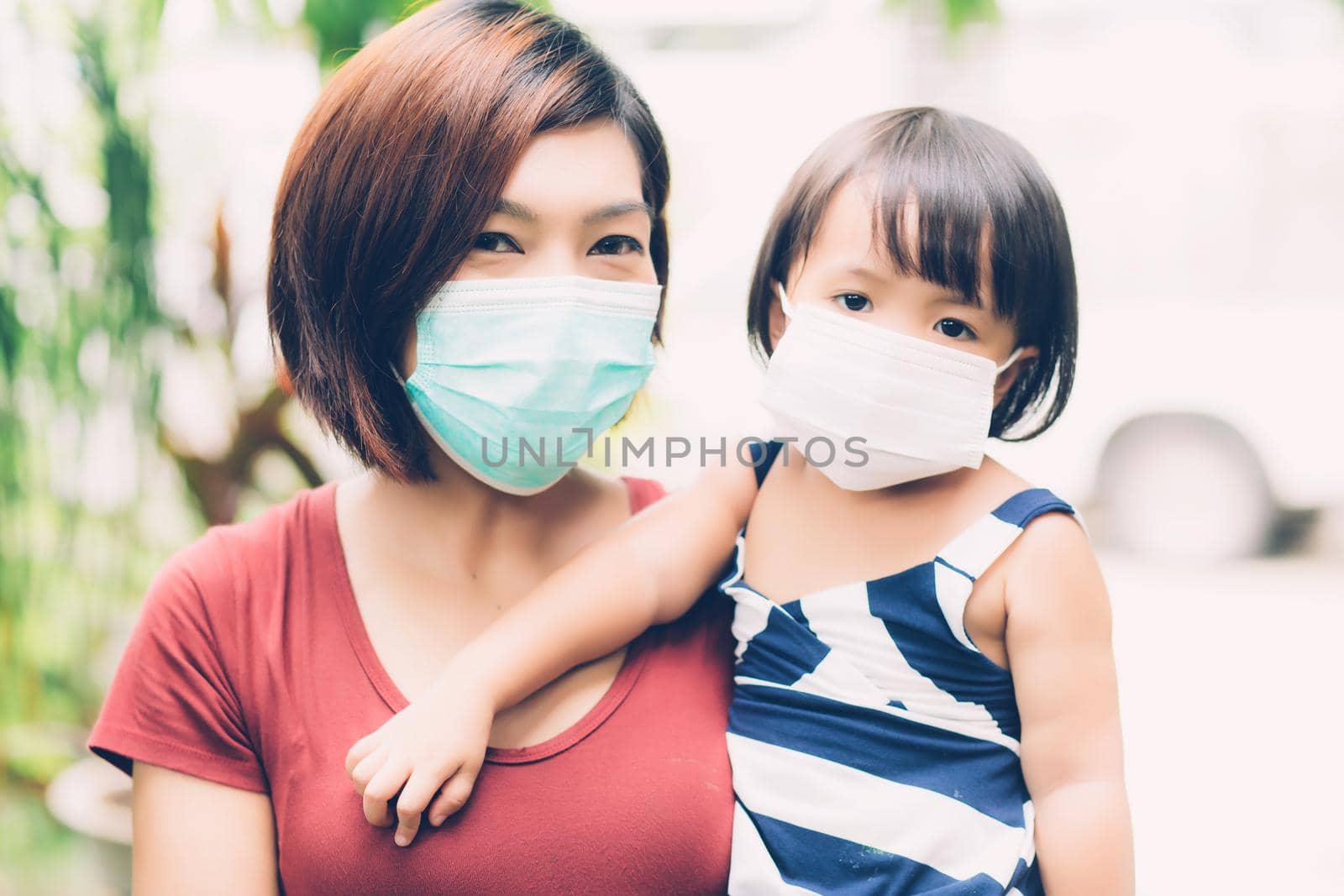 Mother take care daughter with face mask for protection disease flu or covid-19 outdoors, mom wearing on medical mask with child safety for protect outbreak of pandemic, medical concept. by nnudoo