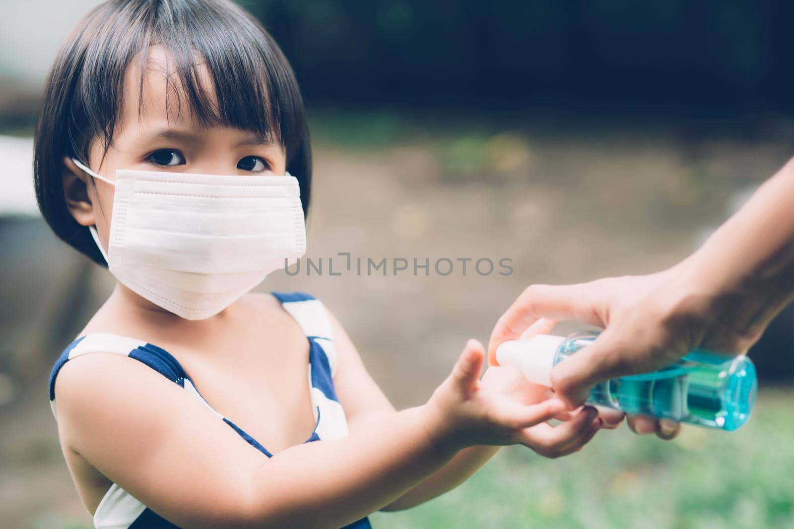 Mother take care daughter with face mask and sanitizer for protection disease flu or covid-19 outdoors, mom and child wearing medical mask clean hand for safety for outbreak of pandemic in public.