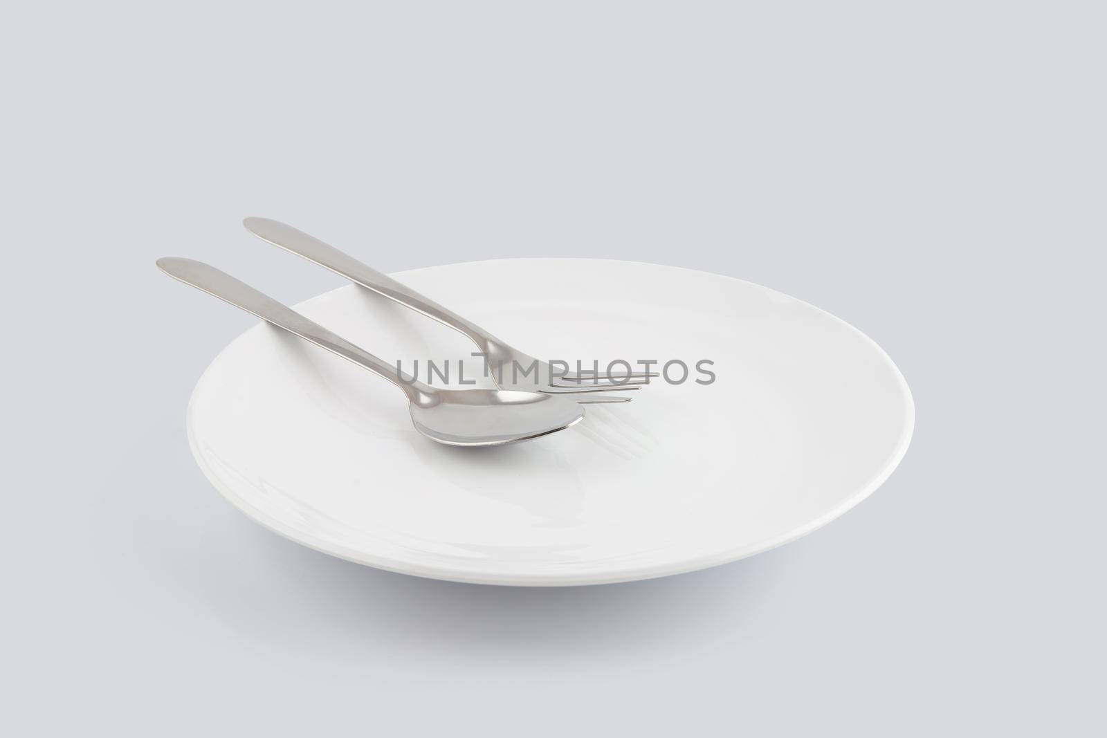 Dish spoon and fork isolated on white background, utensil for food, ceramic plate with empty, kitchenware or dishware with stainless in studio, object concept. by nnudoo