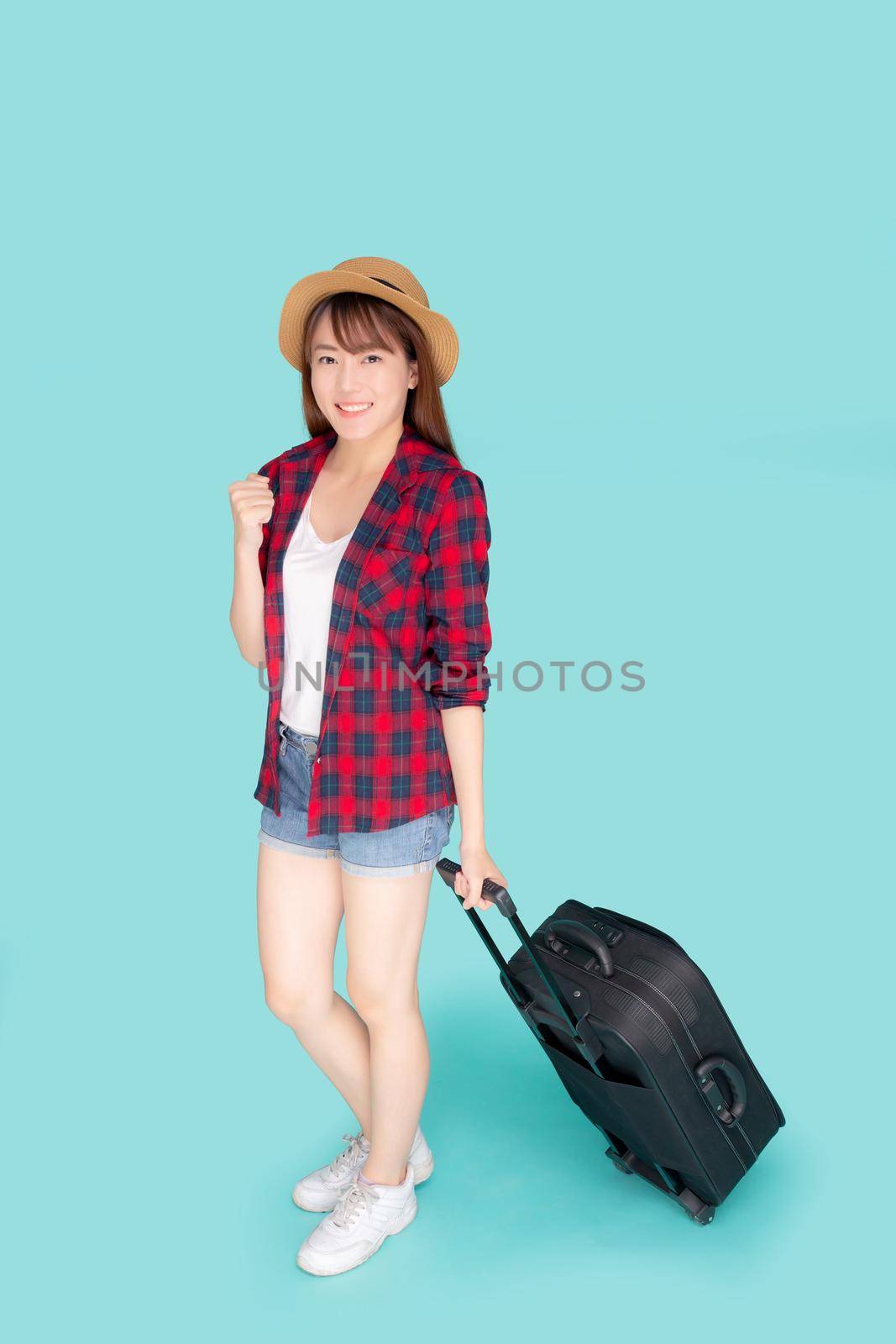 Beautiful young asian woman pulling suitcase isolated on blue background, asia girl having expression cheerful and success holding luggage walking in vacation with excited, journey and travel concept.