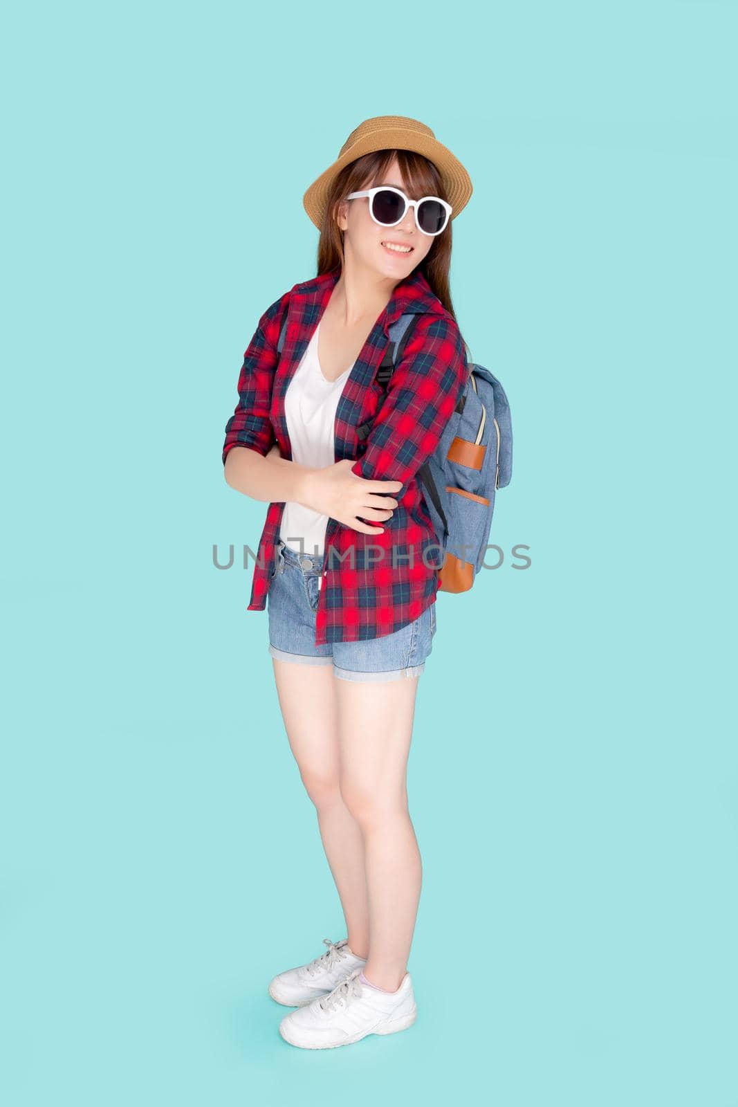 Beautiful portrait young asian woman wear sunglasses and hat smile excited and confident enjoy summer holiday isolated blue background, model girl cheerful having backpack in vacation, travel concept.