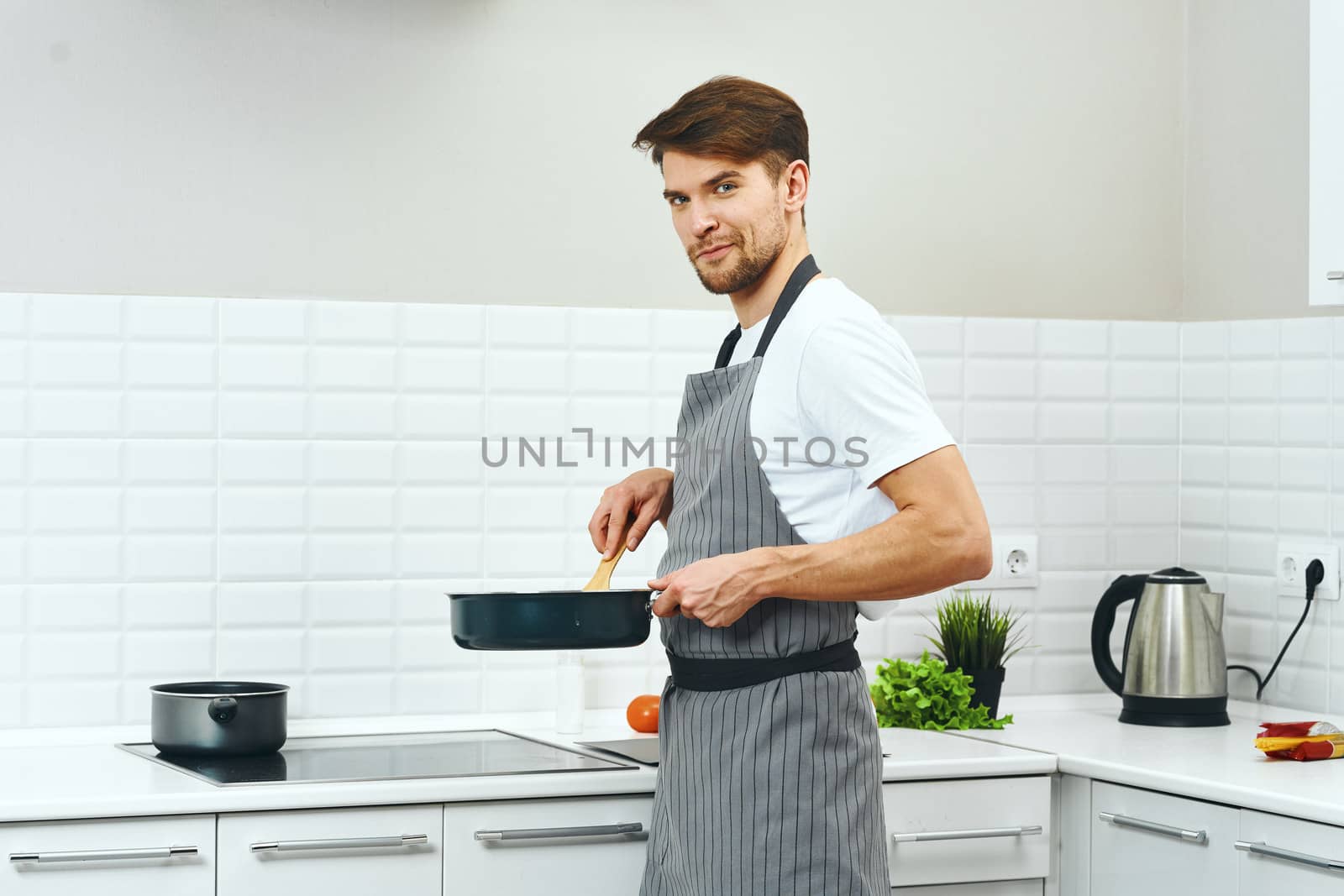 A male chef in gray aprons is holding a frying pan in his hands cooking food kitchen lifestyle