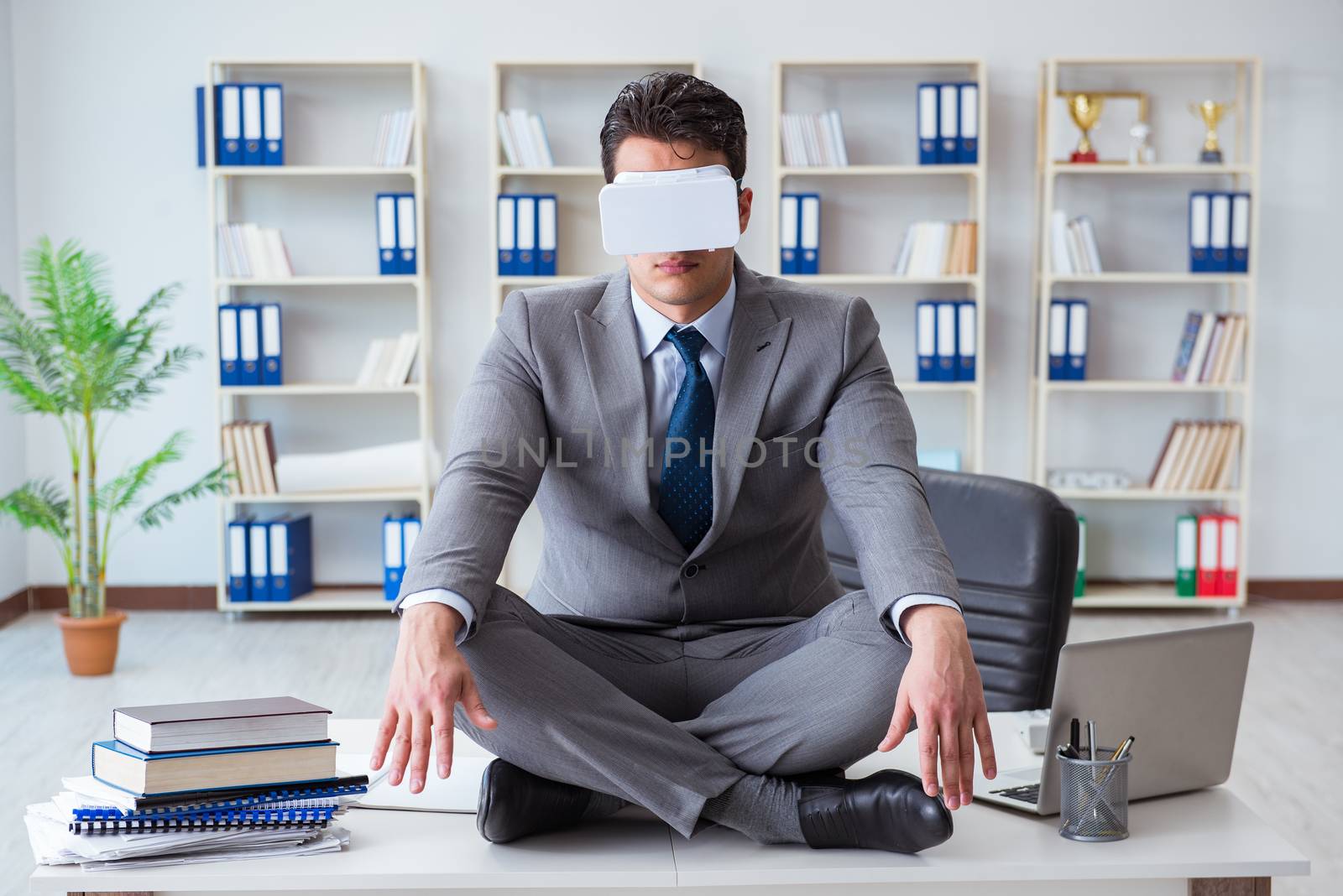 Businessman in virtual reality VR glasses meditating at desk top by Elnur
