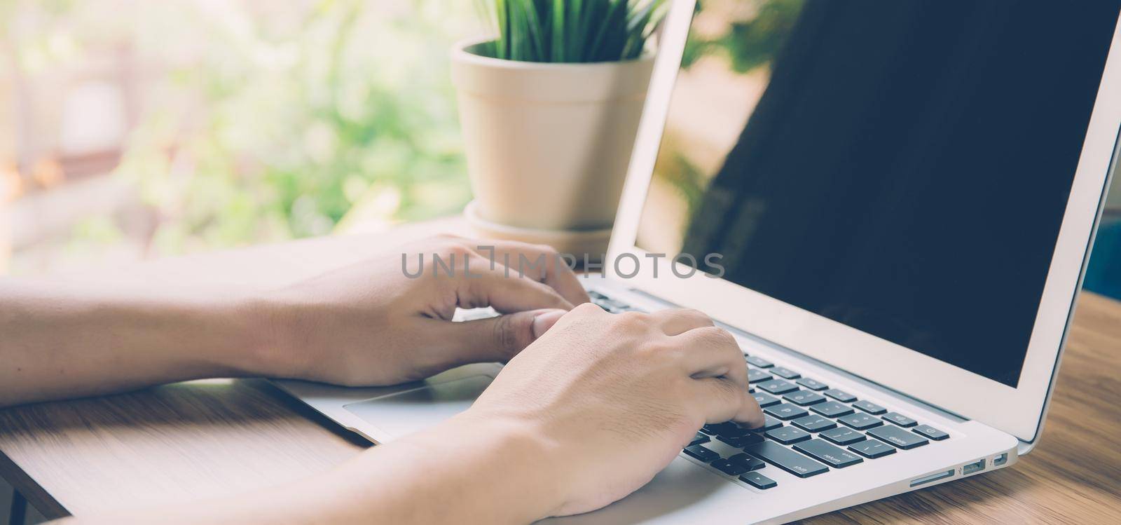 Hand of man working laptop computer with blank screen, work from home for social distracting is new normal, freelance using notebook, business and communication concept, banner website.