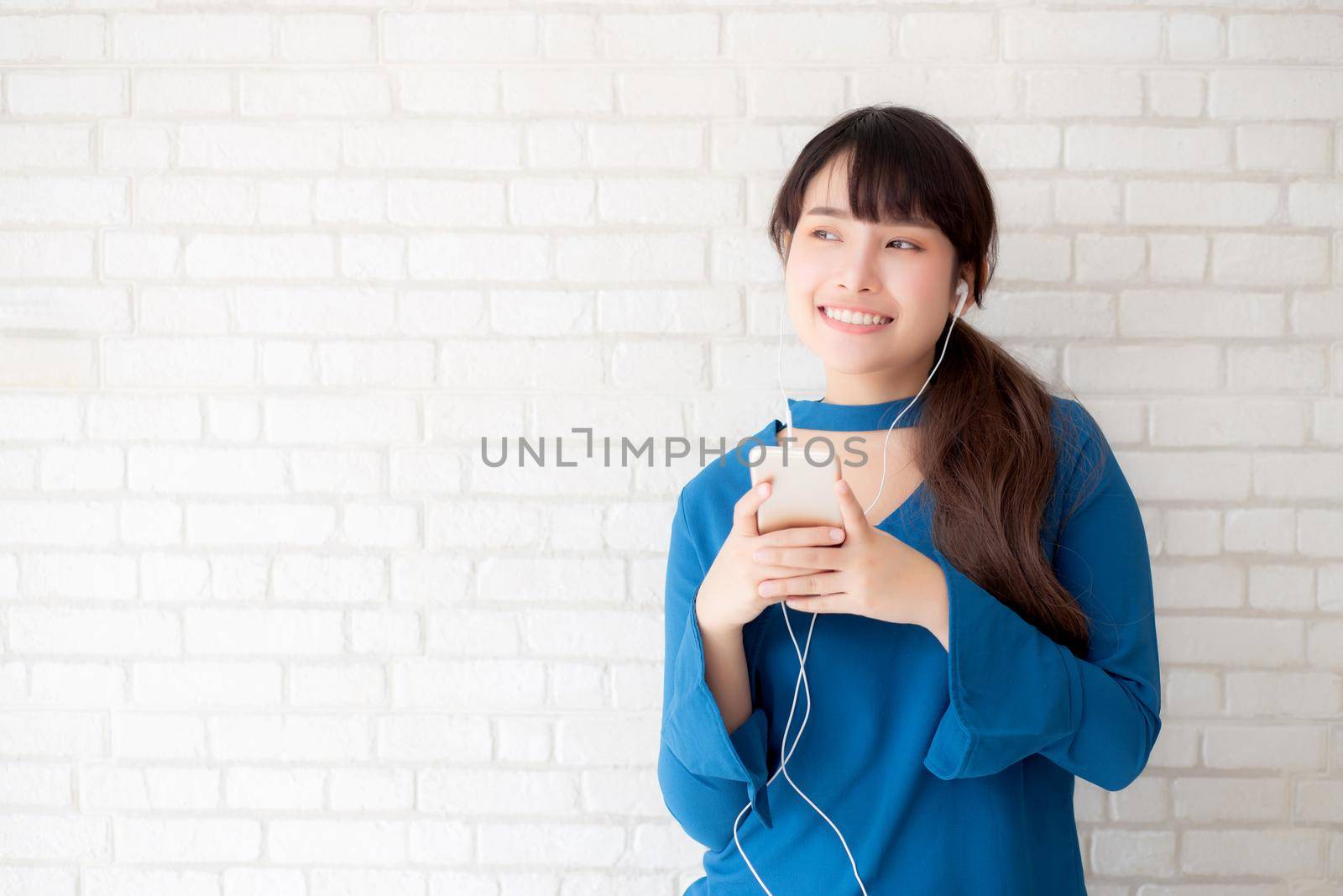 Beautiful portrait asian young woman standing happy enjoy and fun listen music with headphone on cement concrete background, lifestyle of girl relax sound radio with earphone, technology concept.